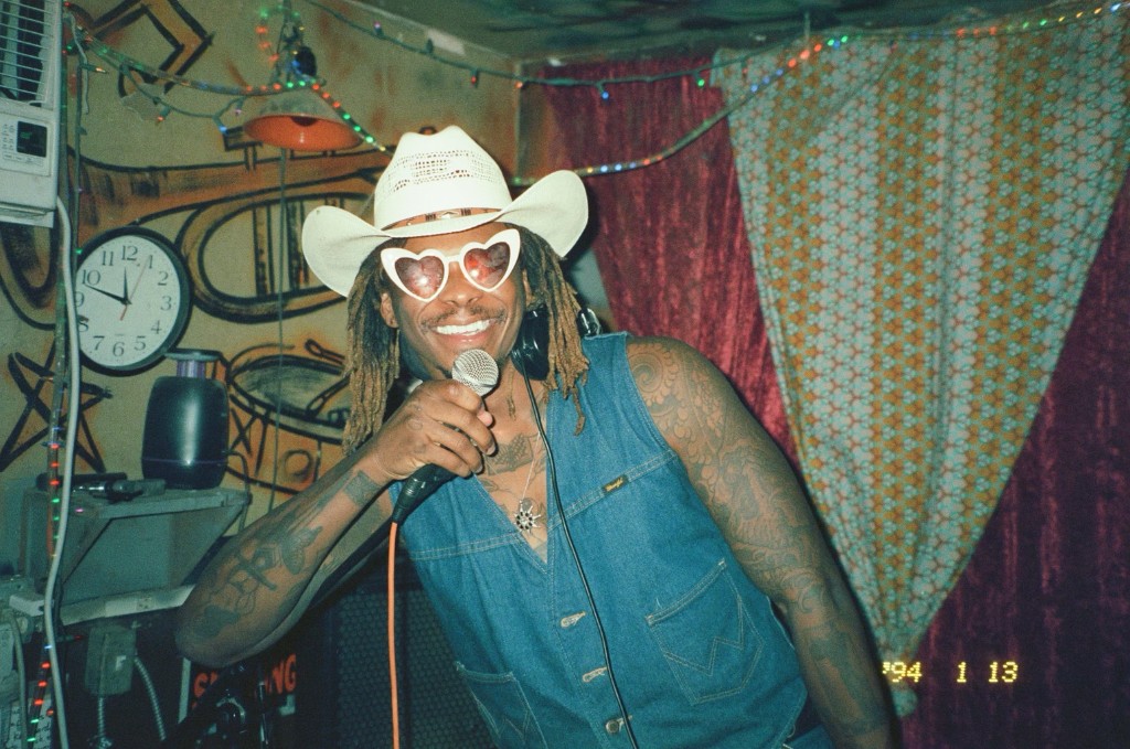 Juan Lo smiling with a microphone in a club